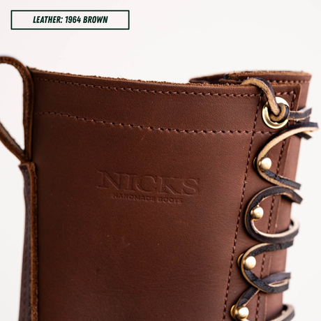 Close-up of a brown leather boot with decorative laces and metal eyelets, showing the embossed brand name 'NICKS HANDMADE BOOTS' and a text label reading 'LEATHER: 1964 BROWN'.