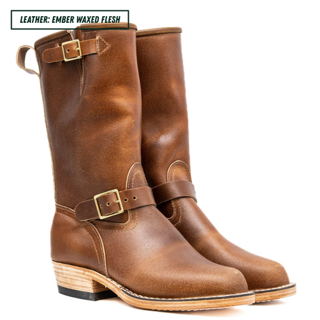A pair of mid-calf leather boots in a warm amber-brown shade, featuring a single strap with a brass buckle across the instep and pull loops at the top. The boots are shown against a plain white background with a text label in the top-left corner reading 'LEATHER: EMBER WAXED FLESH'.