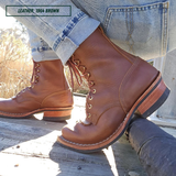 A pair of brown leather lace-up boots worn with cuffed blue jeans, photographed outdoors on a wooden surface. A text overlay in the top left reads 'LEATHER: 1964 BROWN'.