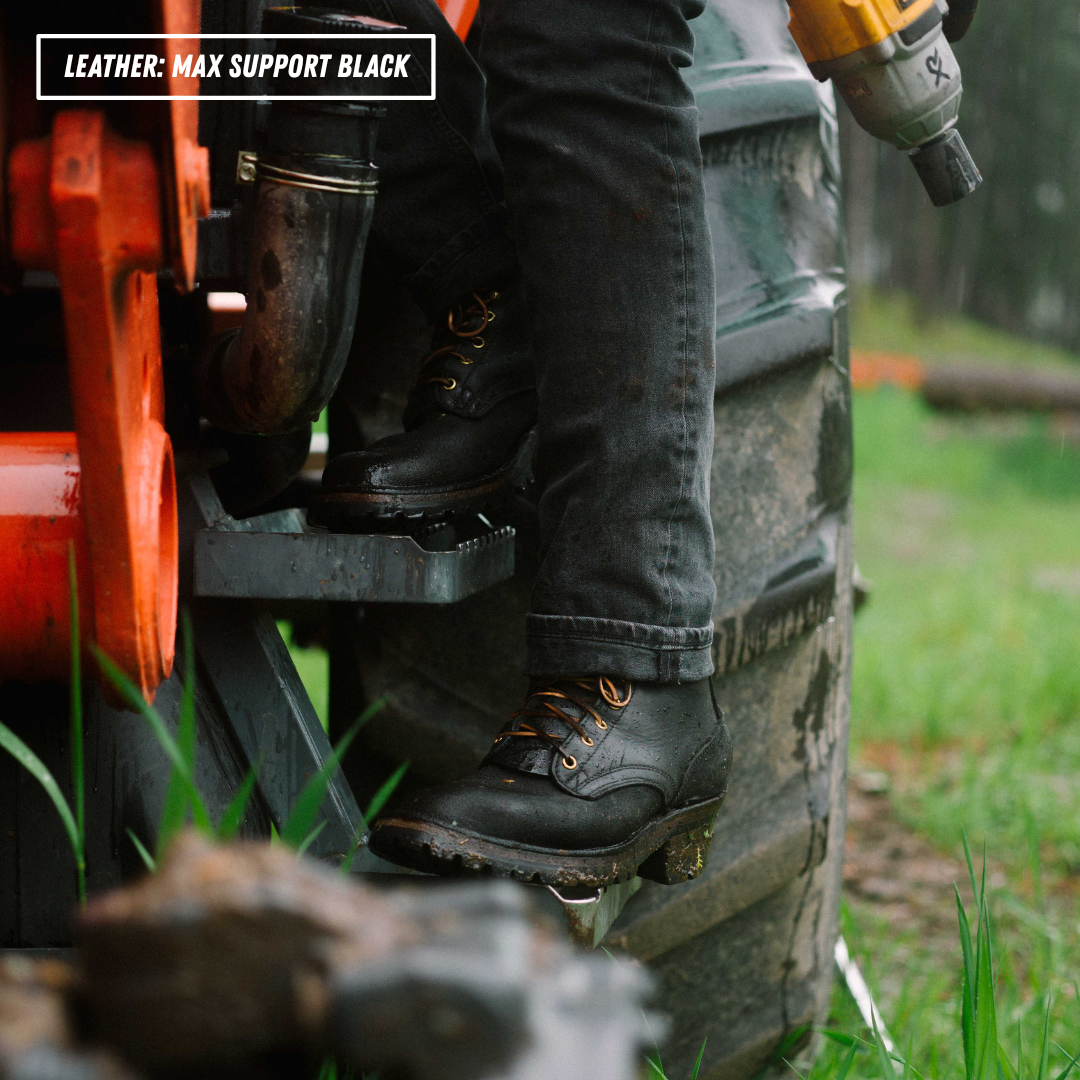 A close-up outdoor shot of a person wearing black leather work boots with orange laces, standing on a tractor step next to a large tire. A yellow cordless drill is visible in one hand, and a text overlay in the top-left reads 'LEATHER: MAX SUPPORT BLACK'.