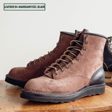 A pair of brown suede lace-up work boots with black leather single piece backstay sitting on wooden table. A text label in the top left reads 'LEATHER:64 MAHOGANY/CXL BLACK'.