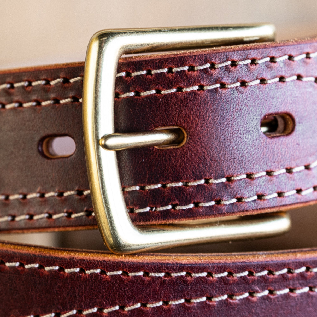 Close-up of a brown leather belt with a gold buckle on a beige background