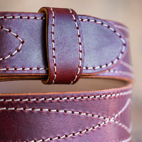 Close-up of a brown leather belt with visible stitching on a wooden surface.