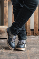 Person wearing dark blue jeans and gray boots on a wooden floor.
