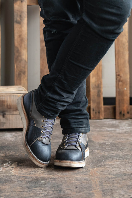 Person wearing dark blue jeans and gray boots on a wooden floor.