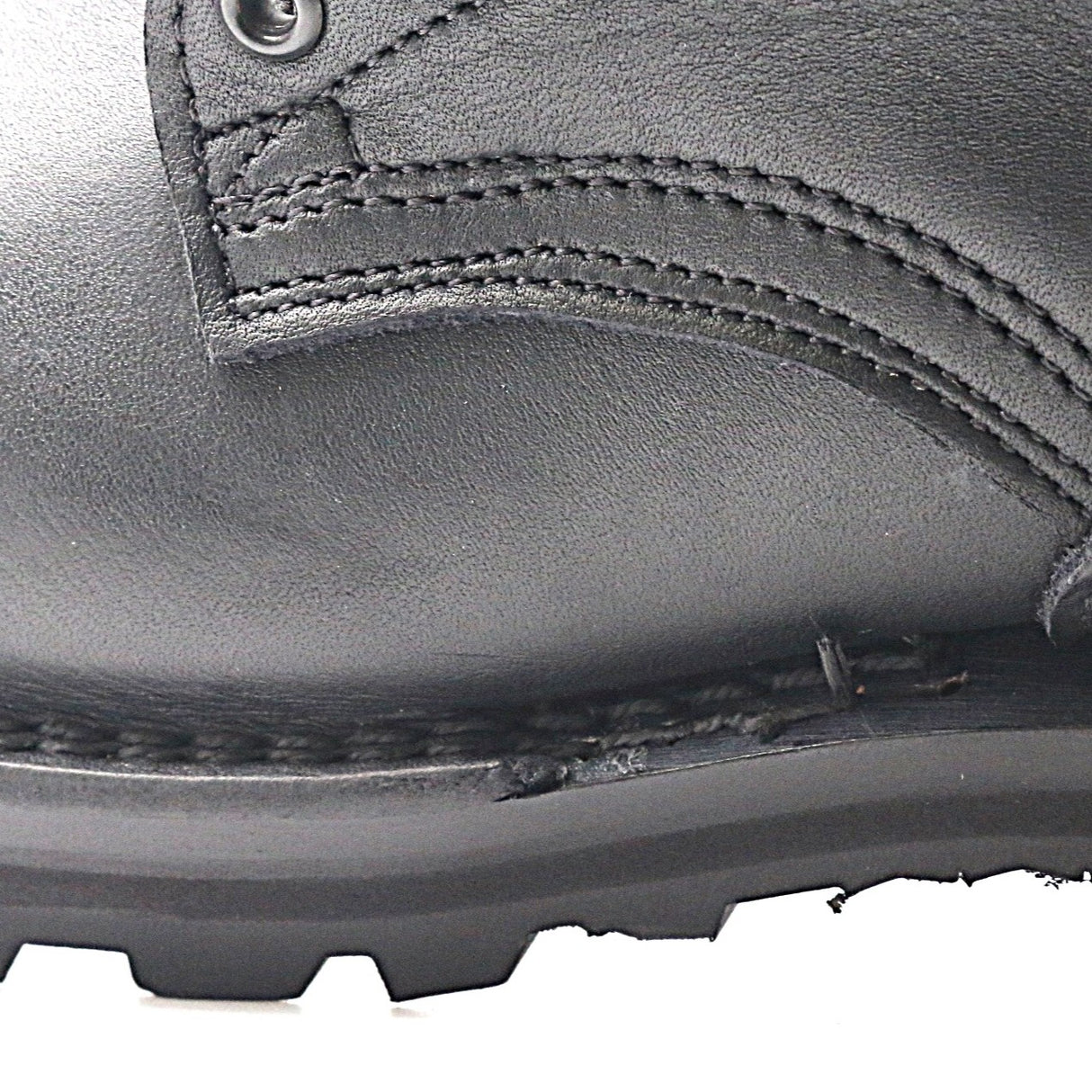 Close-up of a black leather boot showing the side panel, stitching, metal eyelet, and rugged black rubber sole against a white background.