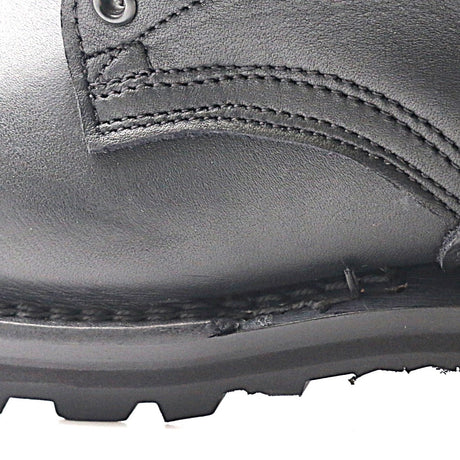 Close-up of a black leather boot showing the side panel, stitching, metal eyelet, and rugged black rubber sole against a white background.