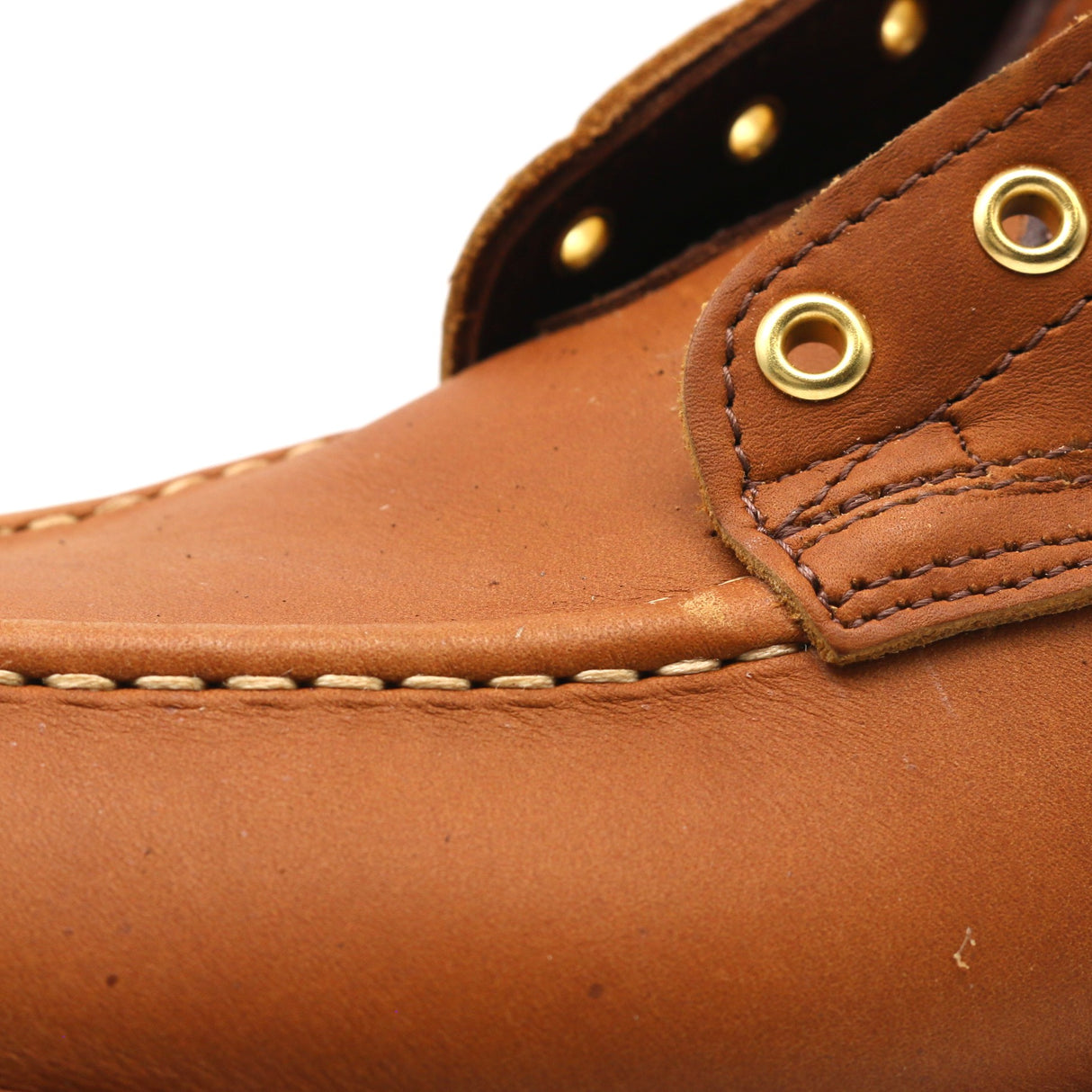 Close-up of a brown leather shoe with gold eyelets on a white background