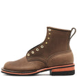 A brown suede lace-up ankle boot with brass eyelets, a pull tab, and a black sole with a copper-orange midsole layer, shown against a plain white background.