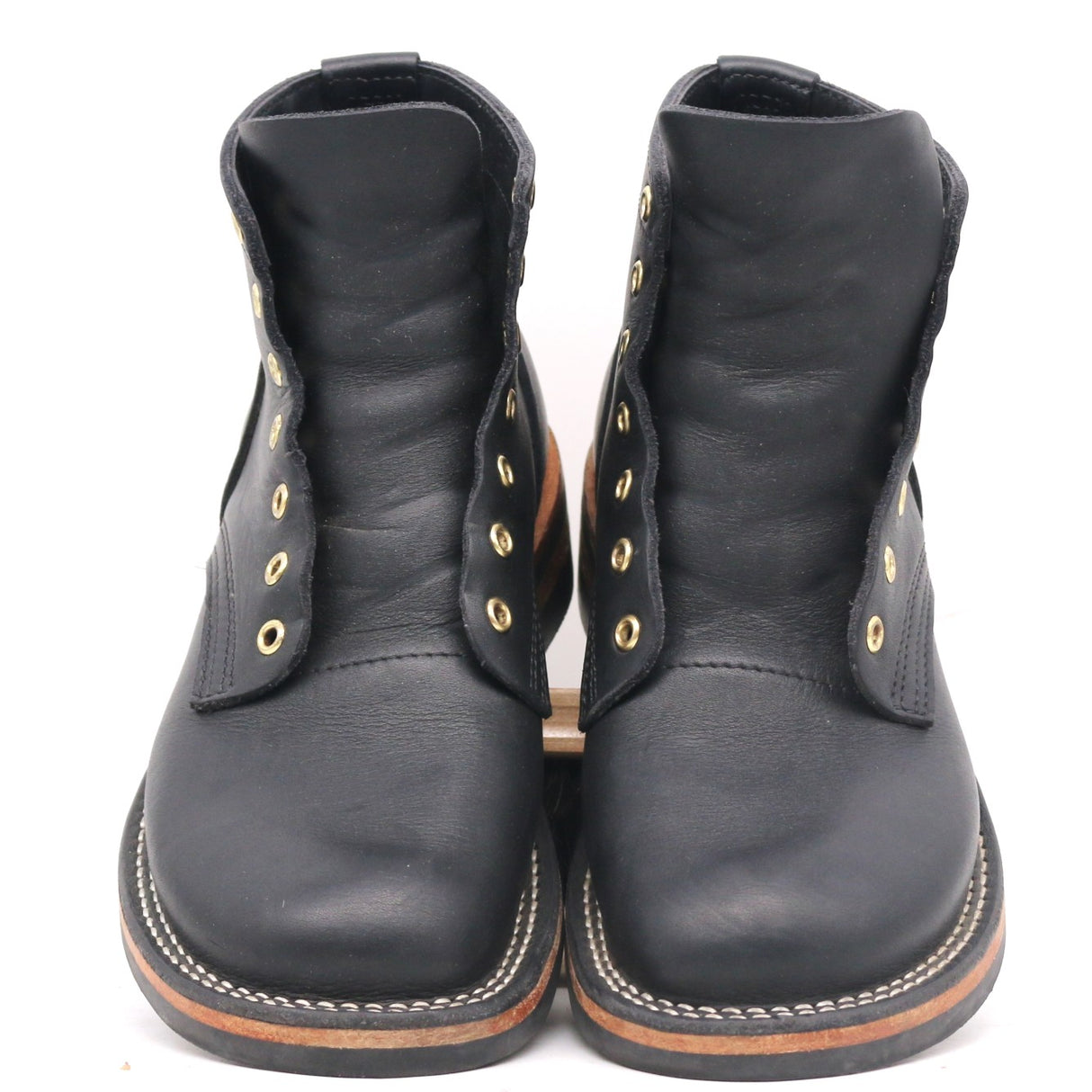 A pair of black leather lace-up ankle boots with gold-tone metal eyelets and white contrast stitching on the soles, shown against a plain white background.