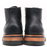 A pair of black leather ankle boots shown from the back, featuring a stacked sole with a brown wood-look layer and a black rubber outsole, set against a plain white background.