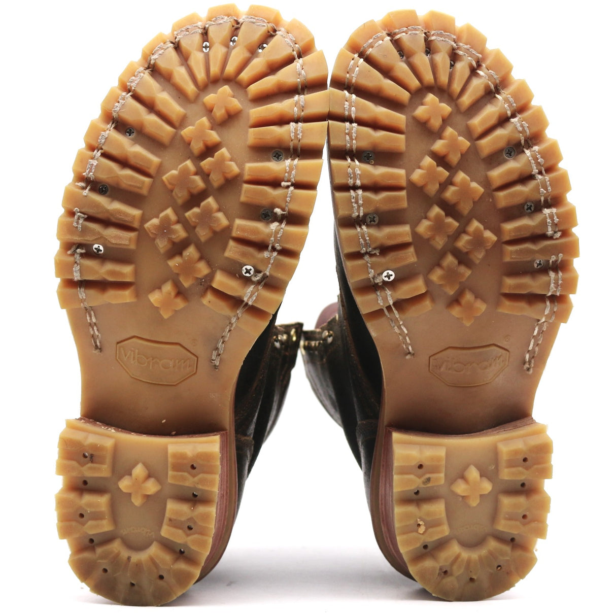 A pair of brown leather boots shown from the sole view, highlighting the deep lugged rubber outsoles and decorative silver metal studs along the stitching.