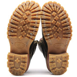 A pair of brown leather boots shown from the sole view, highlighting the deep lugged rubber outsoles and decorative silver metal studs along the stitching.
