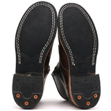 The soles of a pair of dark brown leather boots, showing the black tread, white contrast stitching, and orange rubber protective caps on the heels against a white background.
