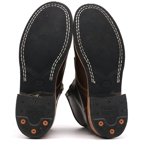 The soles of a pair of dark brown leather boots, showing the black tread, white contrast stitching, and orange rubber protective caps on the heels against a white background.