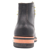 A black leather ankle boot shown from the back, featuring a stacked sole with a black rubber top, a tan mid-layer, and a dark speckled base, accented by gold-tone eyelets.