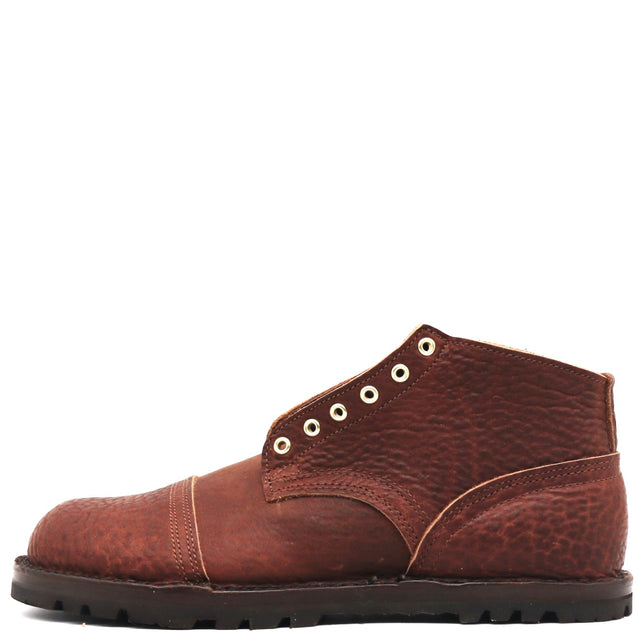 A single brown leather chukka boot with a textured pebbled finish, featuring a cap toe, decorative eyelets, and a thick black lug sole, shown against a plain white background.