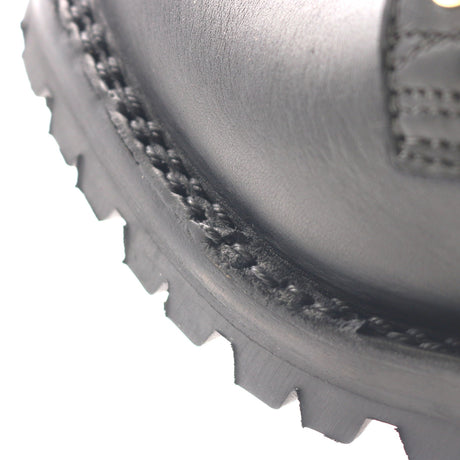 Close-up of a black leather boot corner showing the stitched welt, textured sole edge, and part of the heel on a white background.