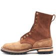 A brown suede and leather lace-up ankle boot with brass eyelets, a pull tab, and a black lug sole, shown from a side profile on a white background.
