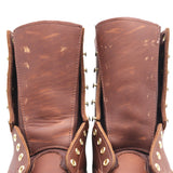 A close-up of a pair of distressed brown leather boots showing the inner shafts, worn leather texture, and brass eyelets and studs.