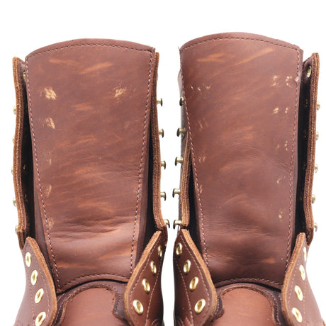 A close-up of a pair of distressed brown leather boots showing the inner shafts, worn leather texture, and brass eyelets and studs.