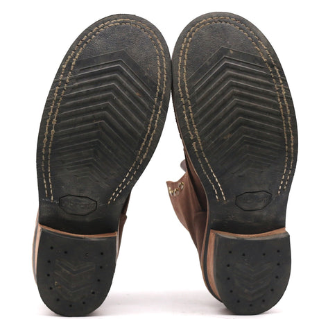 A pair of brown leather boots shown from the bottom, displaying their black treaded soles with white contrast stitching and a textured heel.