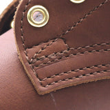 Close-up detail of a brown leather item showing stitched panels, contrast stitching, and a brass snap button.
