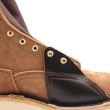Close-up of a brown suede and black leather ankle boot with brass eyelets on a white background.