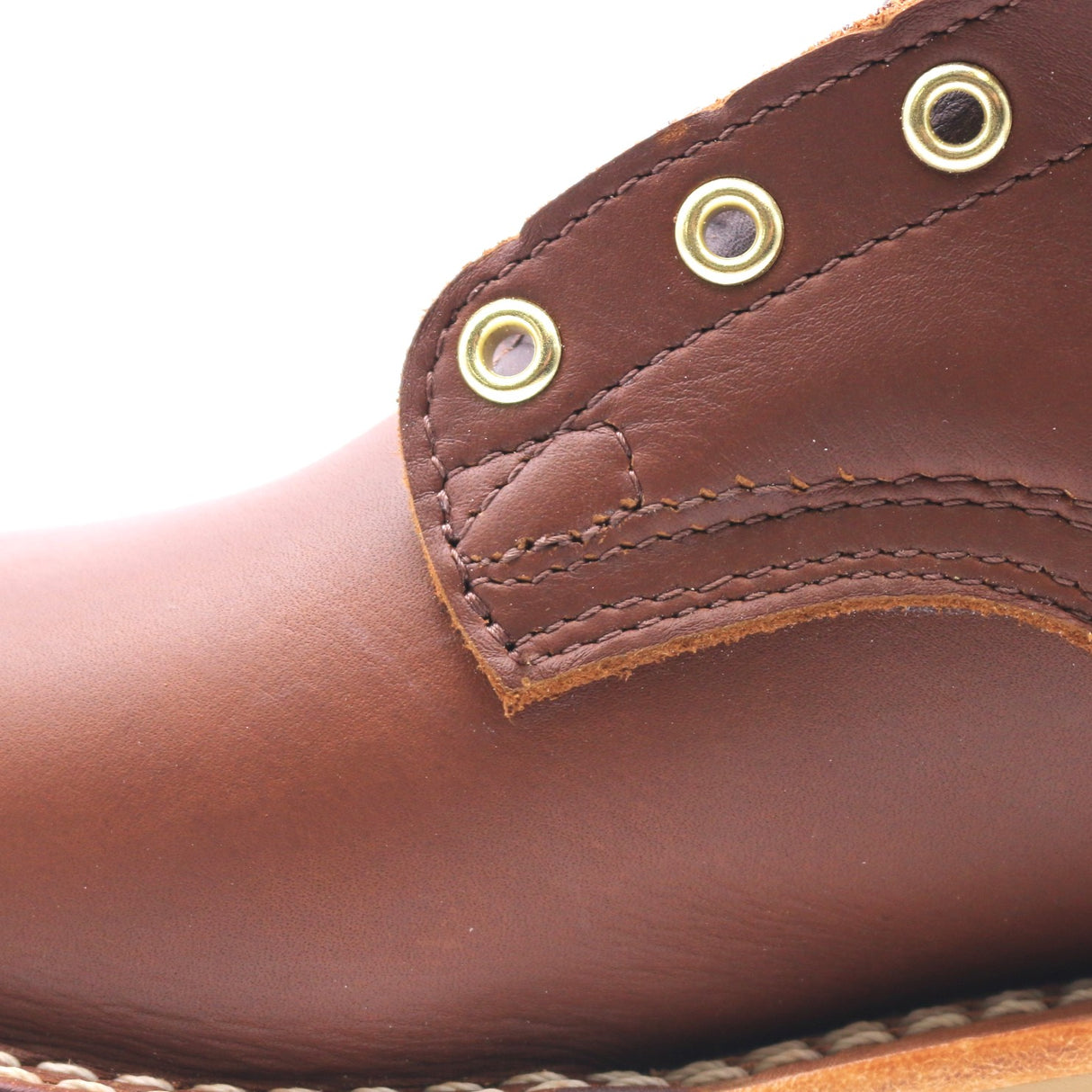 Close-up of a brown leather boot showing the side panel, stitching, and brass eyelets against a white background.