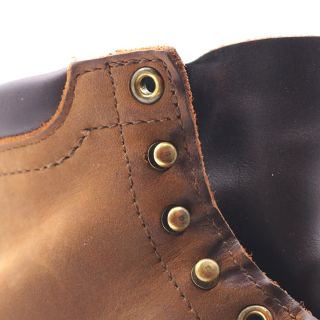 Close-up of a brown leather boot showing the side panel with brass-tone metal eyelets and stitching, next to a dark interior lining.