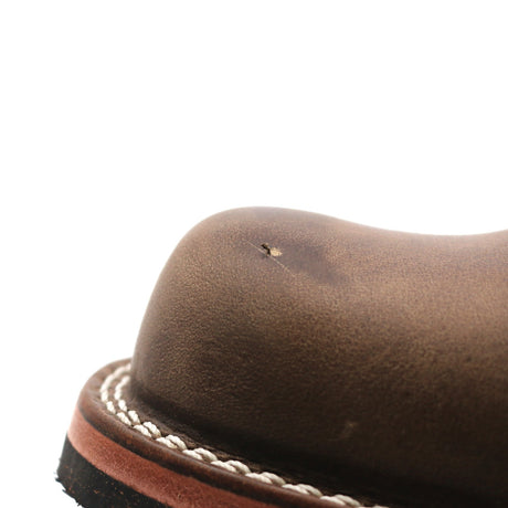 Close-up of a brown leather boot toe showing a small surface defect and white contrast stitching along the edge of a dark sole, on a white background.