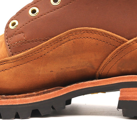 Close-up side view of a brown leather boot showing the side panel, stitching, metal eyelets, and a black lug sole on a white background.