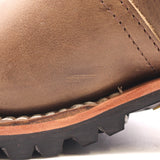 Close-up detail of a brown leather boot showing the side panel, stitching, a tan midsole edge, and a black lug sole.
