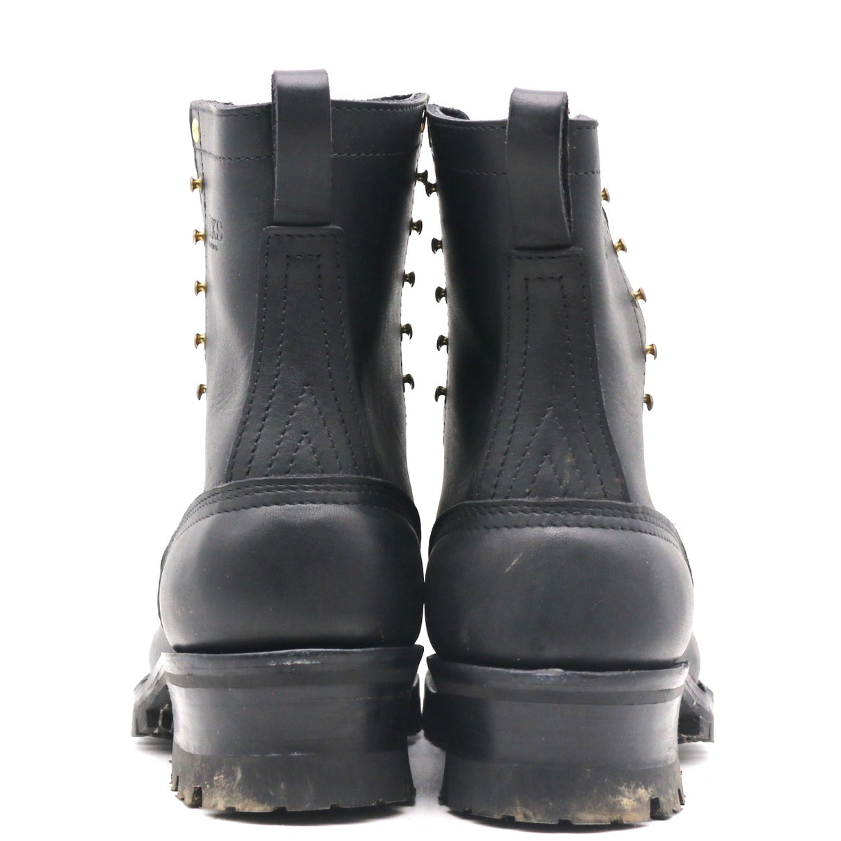 A pair of black leather lace-up ankle boots shown from the back, featuring brass grommets and thick lug soles, set against a plain white background.