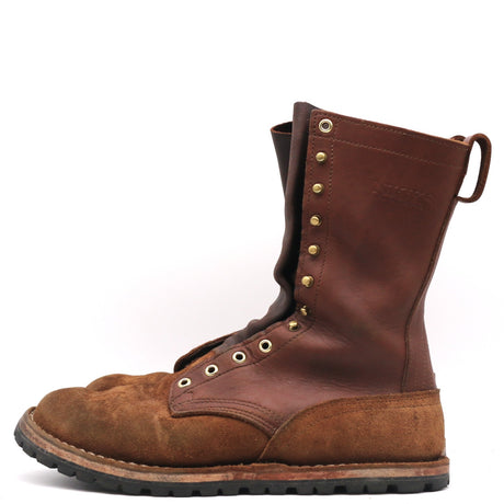 A mid-calf work boot made of dark brown leather and brown suede, featuring brass eyelets, a pull tab, and a thick black treaded sole, shown from a side profile on a white background.