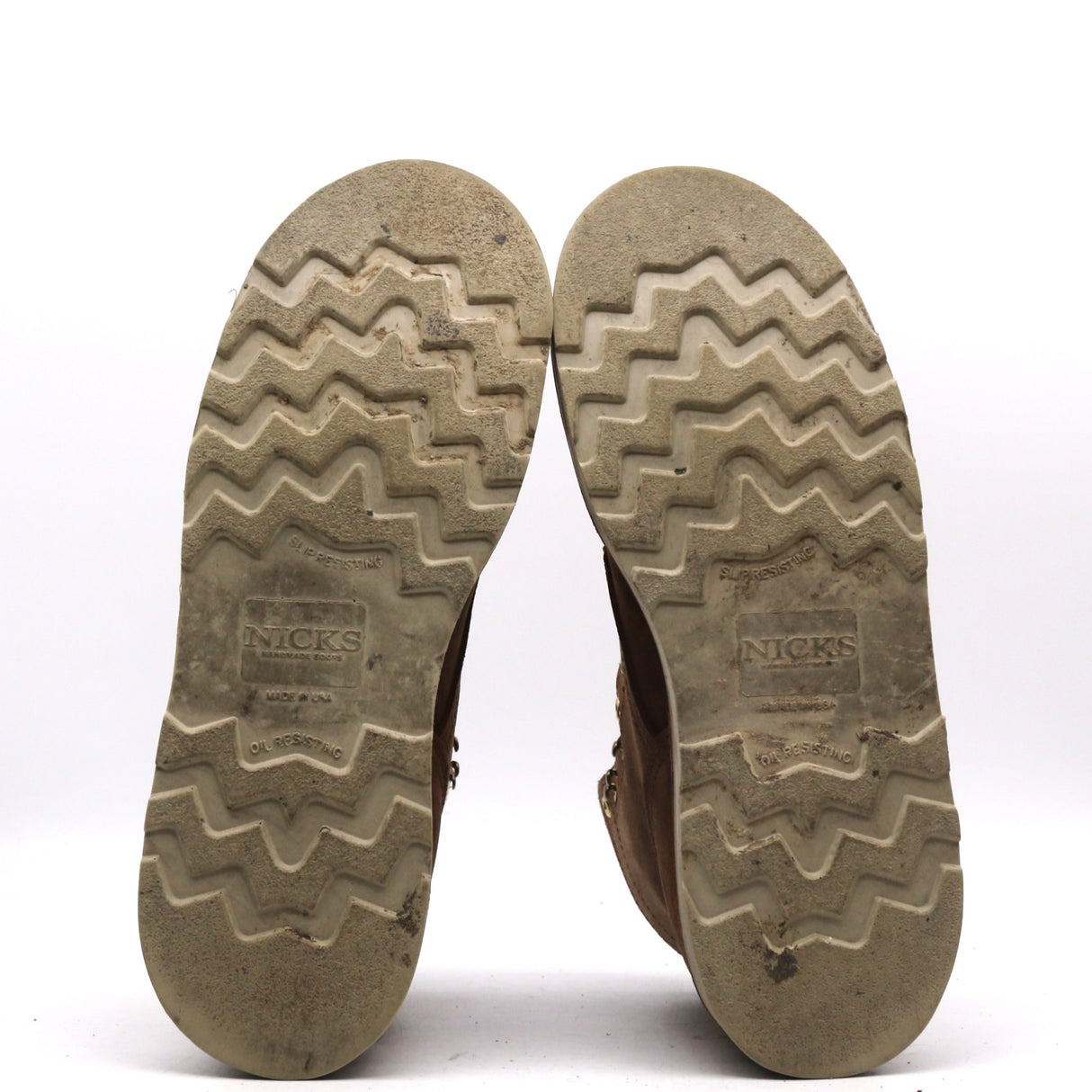 The soles of a pair of brown boots, showing the zigzag tread pattern and the embossed brand name 'NICKS' on a white background.