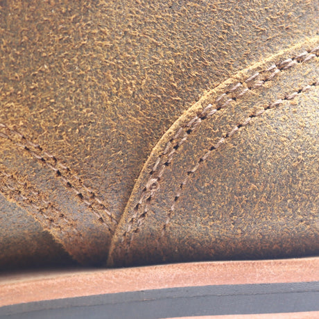 Close-up of a brown leather shoe or boot showing the textured grain, stitching, and a portion of the sole.