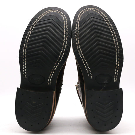 Close-up of the soles of a pair of black leather boots, showing the tread pattern, white contrast stitching, and heel sections on a white background.