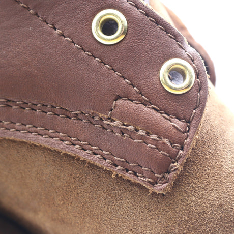 Close-up of a brown leather shoe detail showing contrast stitching, a pull tab, and brass eyelets over a suede-like brown upper.