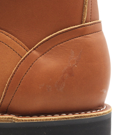 Close-up of a tan leather boot showing the heel and side panel with visible scuffs and dirt marks on the leather surface, set against a white background.