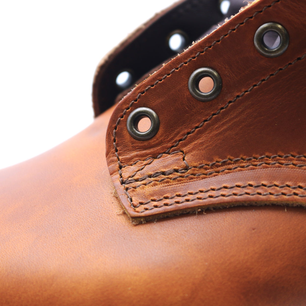Close-up of a brown leather boot showing the side panel, metal eyelets, and stitching against a white background.