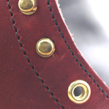 Close-up of a dark red leather strap with black stitching and three brass grommets.