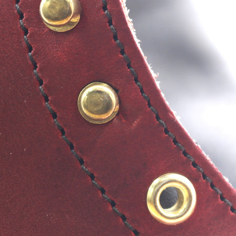 Close-up of a dark red leather strap with black stitching and three brass grommets.