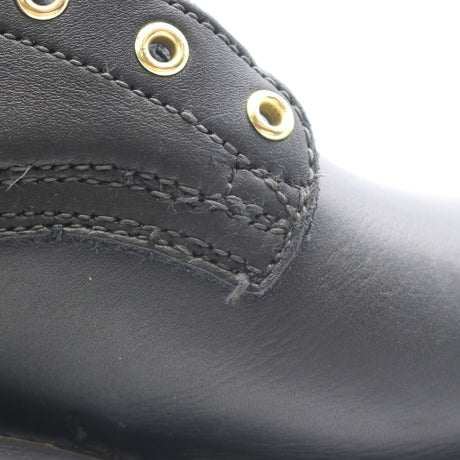 Close-up of a black leather boot showing the side panel with gold-tone metal eyelets and stitching.