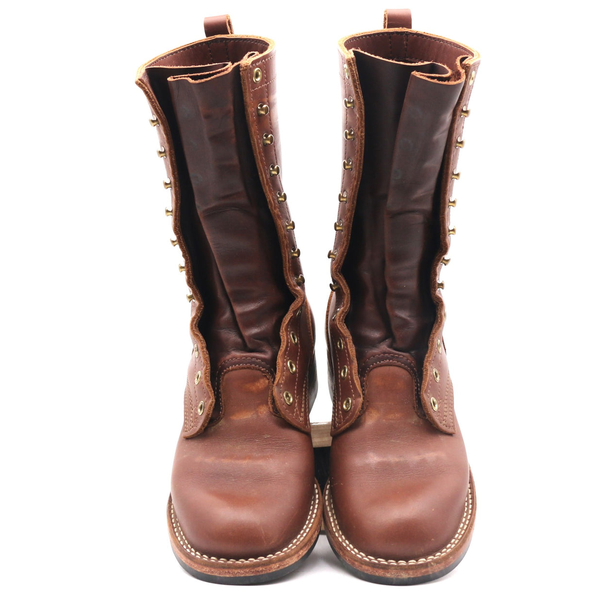 A pair of tall brown leather boots with decorative brass grommets and pull tabs, shown from the front against a plain white background.