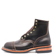 A single black leather ankle boot with gold-tone metal eyelets, contrast stitching, and a stacked sole with a light brown midsole and black outsole, shown against a plain white background.