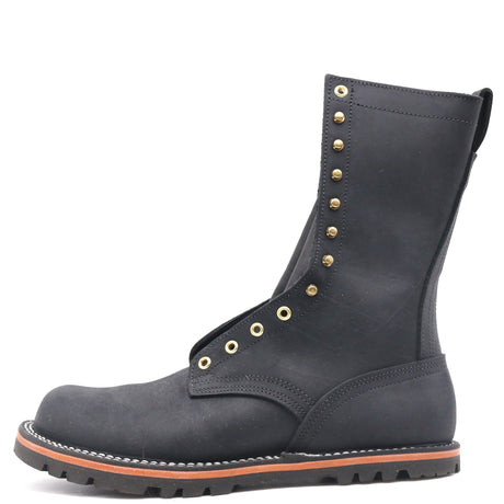 Tall black boot built on a zero-drop flat last with brass hardware in front of a while background.