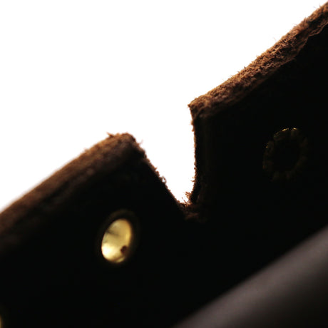 Close-up detail of a dark brown textured leather or felt item with brass-tone rivets against a bright white background.