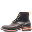 A dark brown leather ankle boot with gold-tone metal eyelets, contrast stitching, and a tan pull loop, shown from a side profile on a white background.