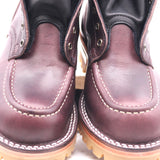 Close-up of a pair of dark burgundy leather boots with white contrast stitching and metal eyelets, shown against a white background.